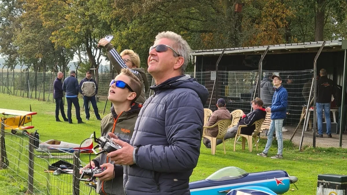 Een jonge modelvlieger krijgt begeleiding met de zender op het clubveld